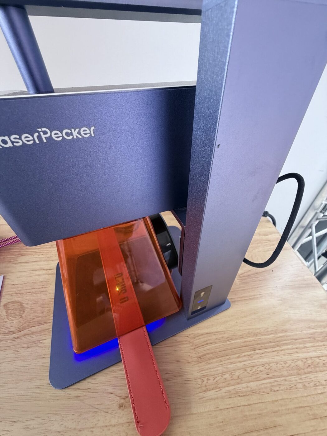 Compact laser engraver marking a red leather strap at the personalization desk