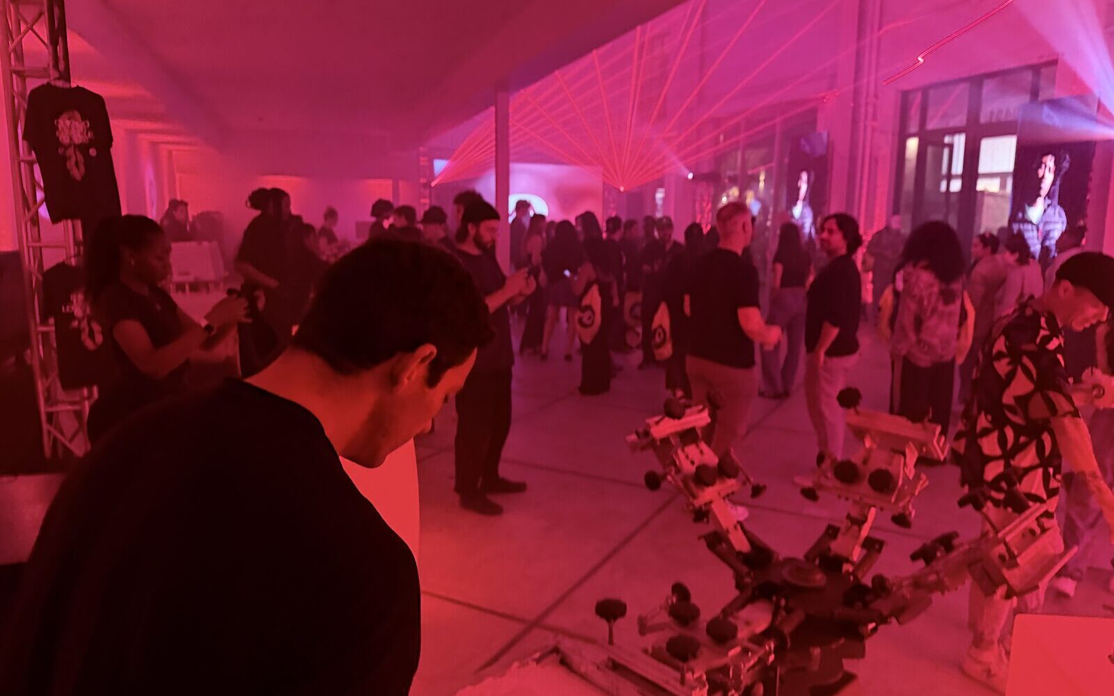Red-lit warehouse party crowd surrounding the customization equipment